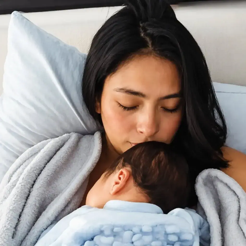 A mother gently kissing her sleeping newborn